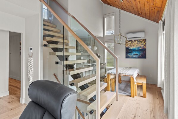 A modern interior with a wooden staircase, a dining area, and a painting on the wall.