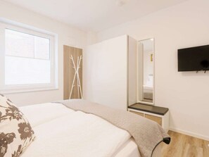 A bedroom with a bed, a bedside table, a mirror, and a TV mounted on the wall. - Holiday Apartment in Greetsiel With Wi-fi (Krummhoern)