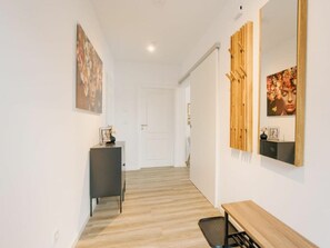 Een gang met een houten vloer, een zwarte console tafel met een fotolijstje en een spiegel met een bloemschilderij.