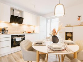 A modern kitchen with white cabinetry, a built-in oven, and a dining area with a round table set for four.