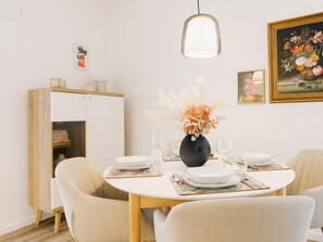 A dining area with a round table, chairs, a vase with flowers, and a cabinet with a light fixture above. - Holiday Apartment in Greetsiel With Wi-fi (Krummhoern)