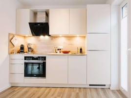 Una cocina moderna con armarios blancos, horno empotrado y cafetera.