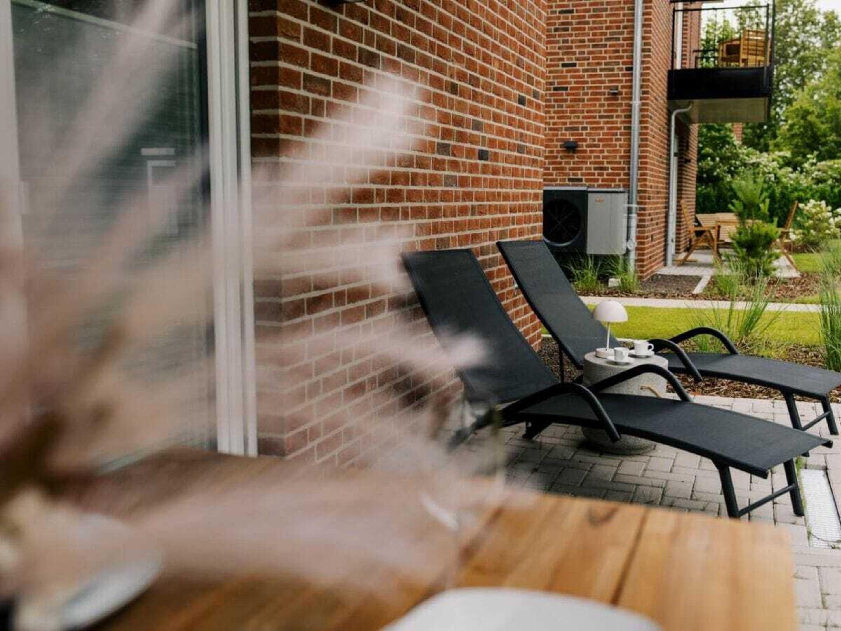 Un patio con dos sillones de descanso y una mesa, un muro de ladrillo y un pequeño jardín con una mesa y sillas.