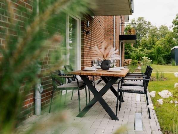 An outdoor patio with a brick wall, a wooden table set for dining, and chairs. - Holiday Apartment in Greetsiel With Wi-fi (Krummhoern)