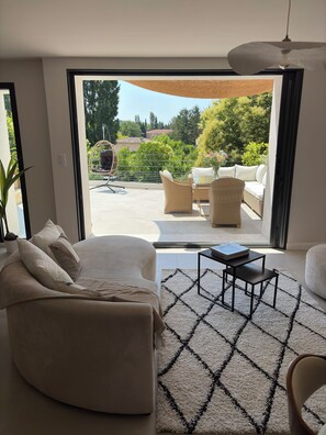A modern living room with a large sliding glass door leading to an outdoor patio area. - MAISON BÂO: A RETREAT OF SOFTNESS AND ELEGANCE (Saint-Cannat)