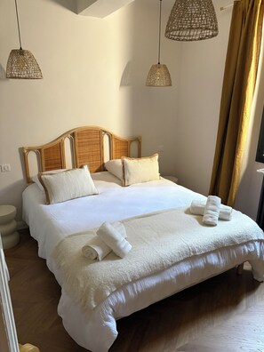 A neatly made bed with white linens and rolled towels, a wooden headboard, and two hanging wicker lamps. - MAISON BÂO: A RETREAT OF SOFTNESS AND ELEGANCE (Saint-Cannat)