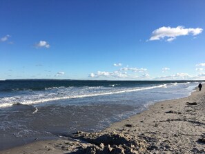 Ein Strand mit Wellen, einem klaren Himmel und einer Person, die spazieren geht.