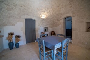 A rustic dining room with a stone wall, a table with chairs, and a door. - Trullo Sippuddo (Puglia)
