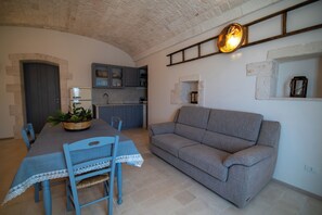 Een eetgedeelte met een tafel, stoelen en een bank. Achtergrond is een keuken met kasten en een spoelbak.