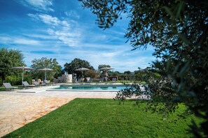 A swimming pool with lounge chairs and umbrellas, surrounded by a stone patio and greenery. - Trullo Sippuddo (Puglia)