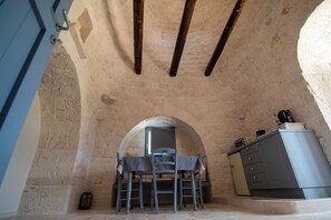 A rustic kitchen with exposed beams, a table with chairs, and a cabinet. - Trullo Sippuddo (Puglia)