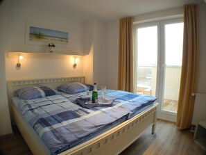 Ein Schlafzimmer mit einem Bett, einem Nachttisch, einem Fenster mit Vorhängen und Blick ins Freie.