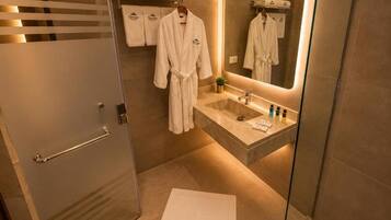 Ein modernes Badezimmer mit einer Duschkabine aus Glas, einem Waschtisch mit Spiegel und einem Handtuchhalter mit Bademänteln.