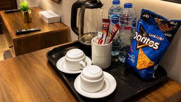 Una bandeja con dos tazas blancas, una cafetera, una taza con un paquete rojo, dos botellas de agua y una bolsa de Doritos.