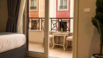 A bedroom with a bed, a sliding glass door leading to a balcony with a table and chairs, and a potted plant.
