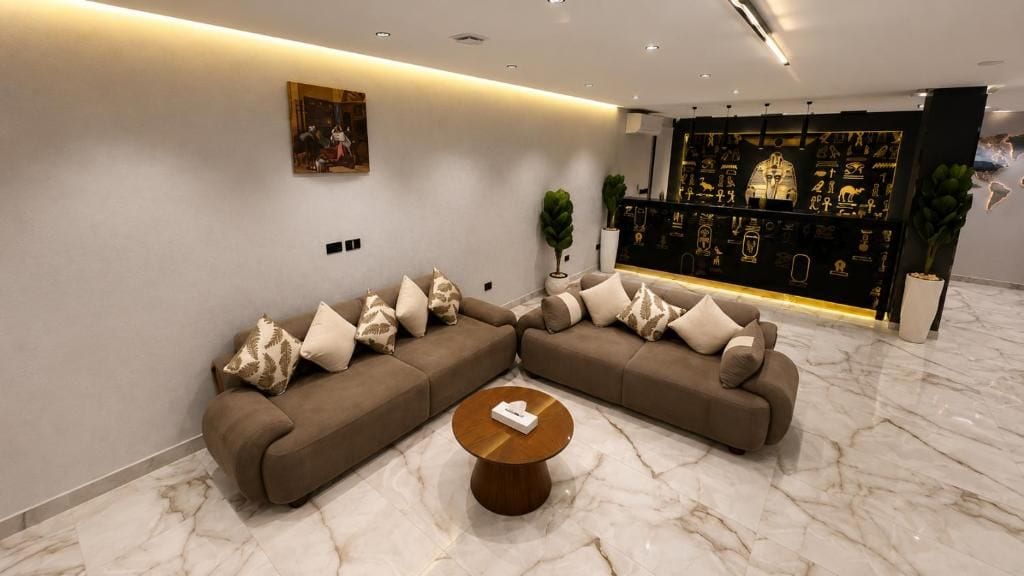 Un salon moderne avec un canapé d’angle, une table basse ronde et un mur décoratif orné d’hiéroglyphes.