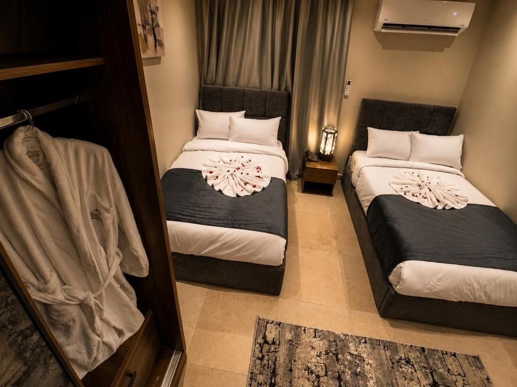 Habitación de hotel con dos camas, un perchero para bata y una mesita de noche con lámpara.