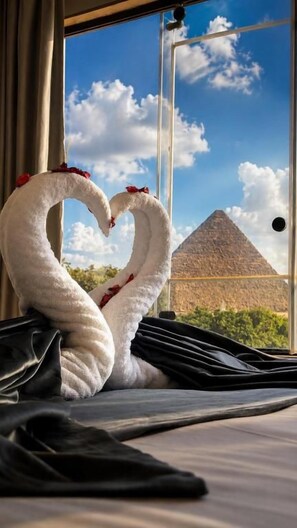 A bed with a view of a pyramid through a window, a swan-shaped towel, and a door. - Terrace Pyramids View (Giza)