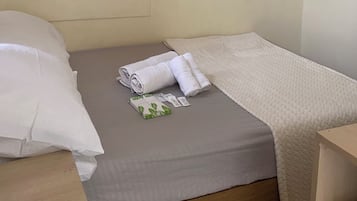 A single bed with a beige blanket and rolled towels.