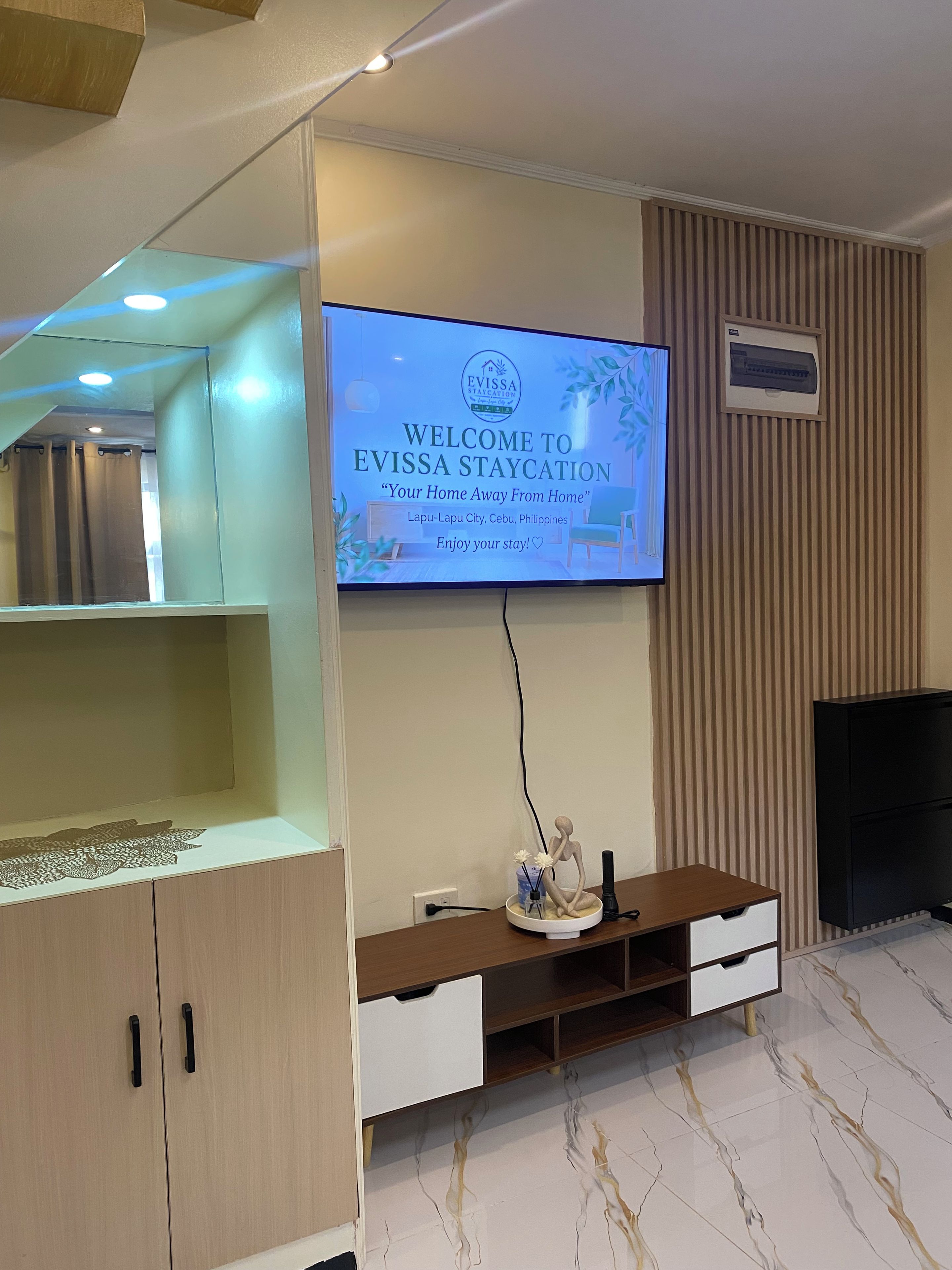 A modern living room with a flat-screen TV displaying a welcome message, a wooden entertainment unit, and a patterned floor.