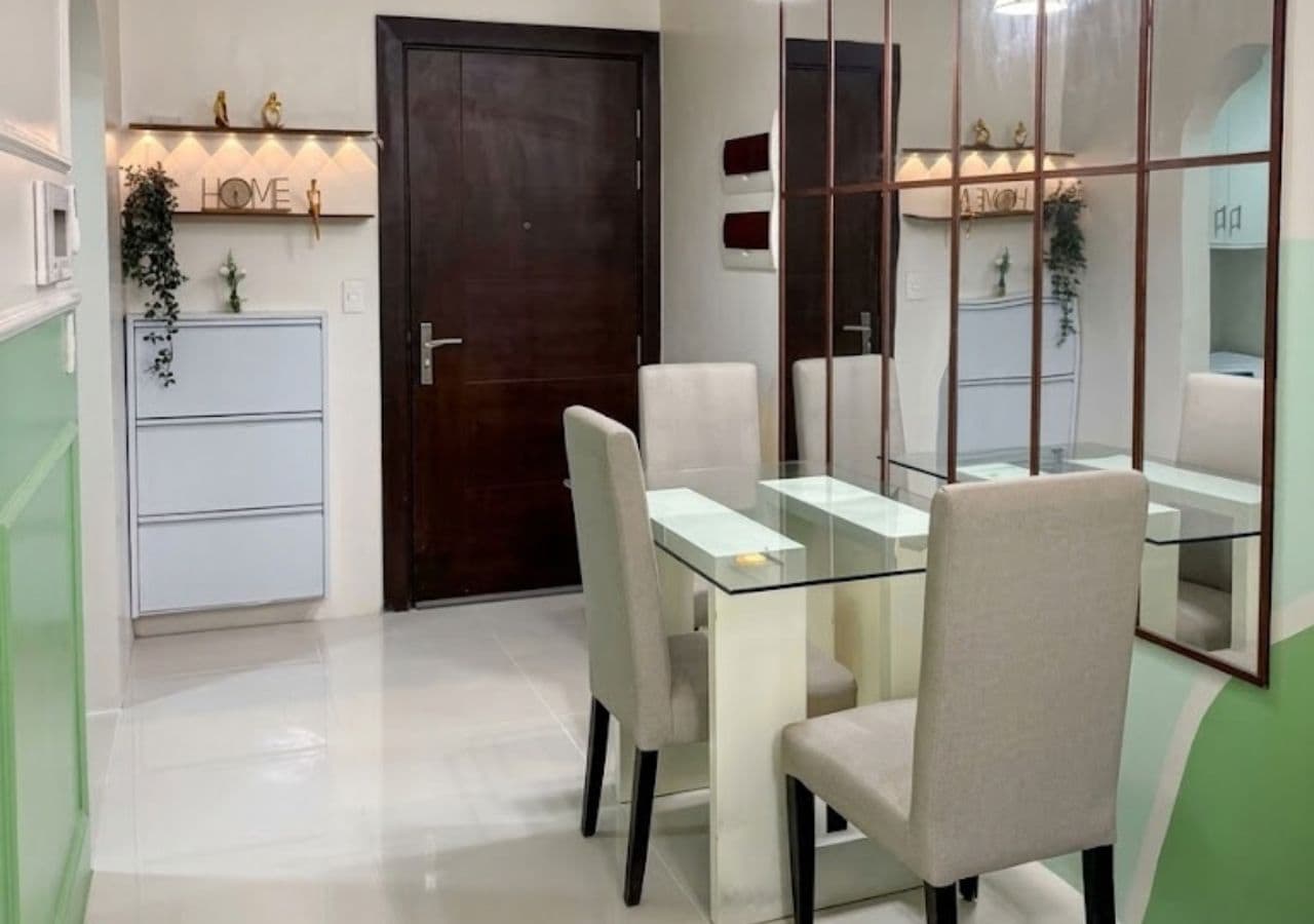 Un comedor con mesa y sillas de vidrio, una puerta de madera y un espejo que refleja la habitación.