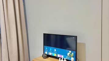 A room with a television on a wooden cabinet, a clock on the wall, and a curtain on the window.