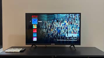 Un televisor sobre un soporte negro, con la interfaz de Netflix en la pantalla, un termostato blanco arriba y un mueble de entretenimiento negro debajo.