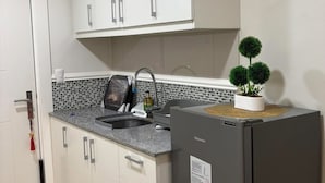 Una cocina compacta con armarios blancos, encimera de granito, lavamanos integrado y un refrigerador pequeño.