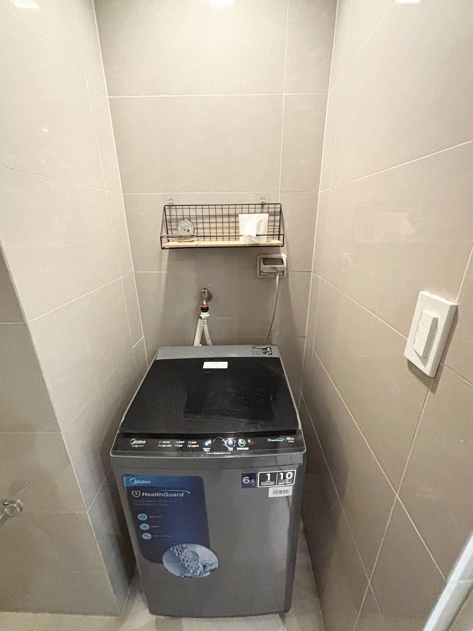 Una unidad compacta de lavadora y secadora empotrada, con un panel de control, un estante pequeño arriba y un enchufe en la pared.