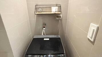 Una unidad compacta de lavadora y secadora empotrada, con un panel de control, un estante pequeño arriba y un enchufe en la pared.