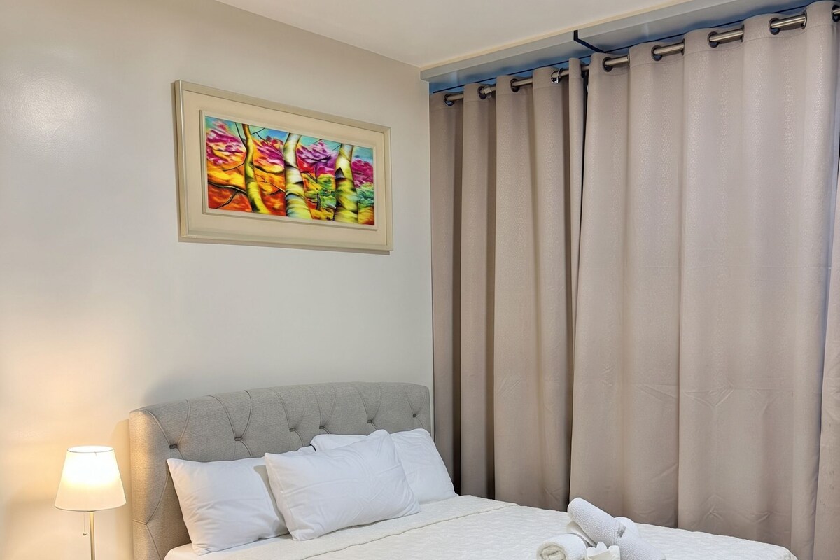 A neatly made bed with white linens, a bedside lamp, and a painting on the wall.