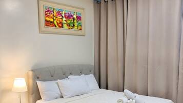 Una cama bien hecha con sábanas blancas, una lámpara de noche y un cuadro en la pared.