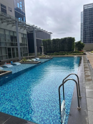 A swimming pool with a tiled deck and a metal ladder. - COZI Uptown Parksuites (Taguig)