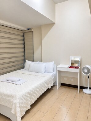 Un dormitorio con cama, mesita de noche y ventilador de pie.