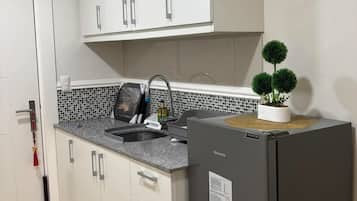 A compact kitchen with white cabinets, a granite countertop, a built-in oven, and a small potted plant.