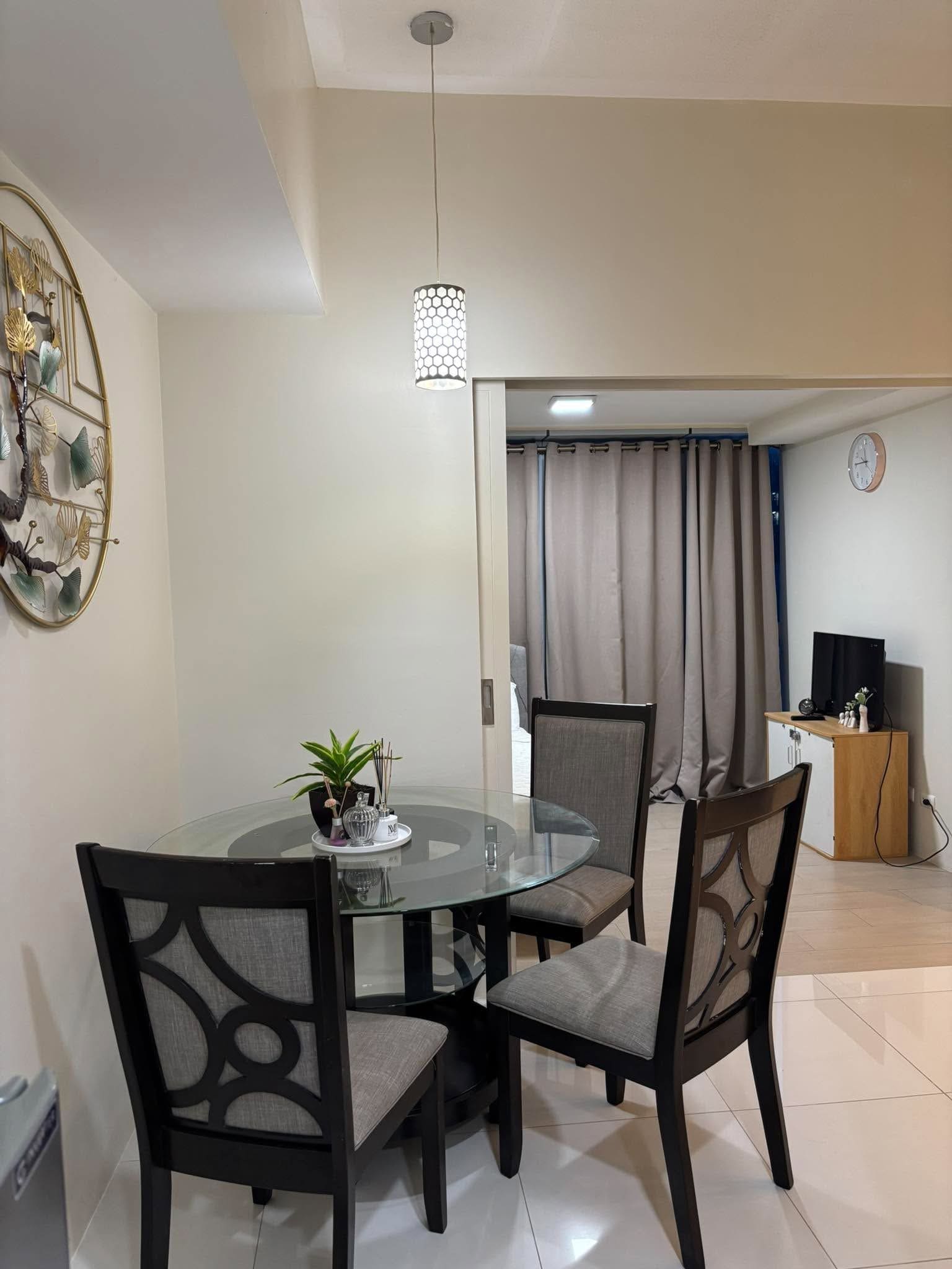 Un comedor con mesa de vidrio, dos sillas, un adorno en la pared y una lámpara colgante.
