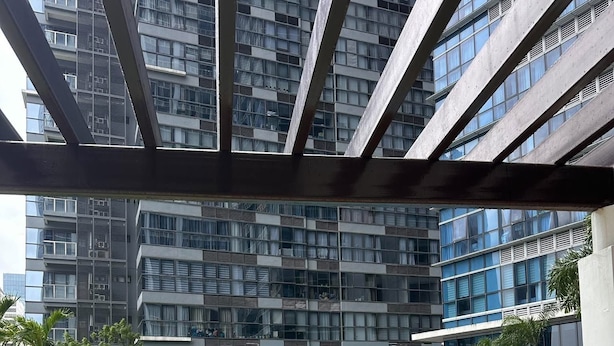 Una piscina con una zona verde circundante, un edificio moderno con balcones al fondo y un cielo despejado.