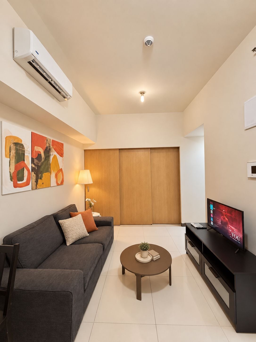 A modern living room with a grey sofa, a coffee table, a TV, and an air conditioning unit mounted on the wall.