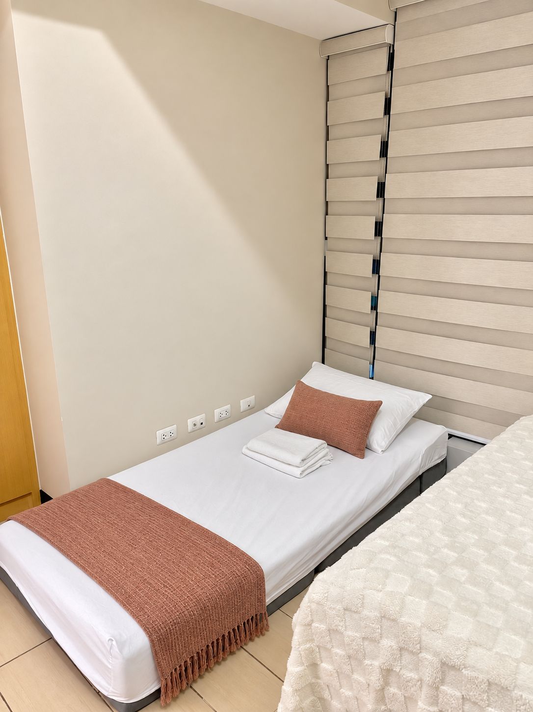 Una cama individual con colchón blanco, manta marrón y almohada blanca.