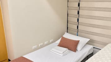 Una cama individual con colchón blanco, manta marrón y almohada blanca.