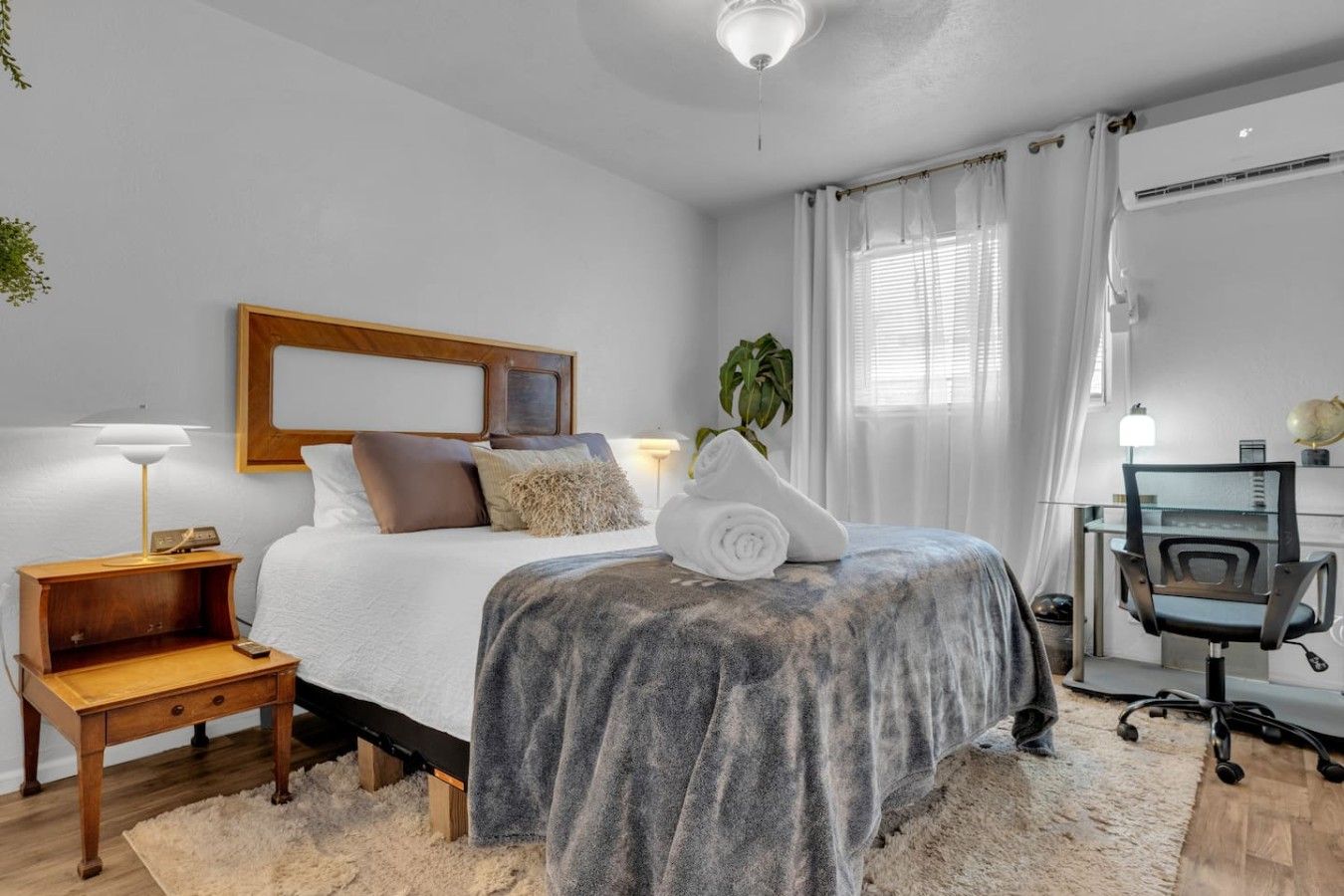 A bedroom with a bed, bedside table, lamp, and a desk with a chair.
