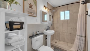 A modern bathroom with a toilet, sink, shower, and a shelf with towels. - Central 2BR | Workspace, Laundry & Long Stays (El Paso)