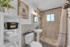 Une salle de bain moderne équipée de toilettes, d’un lavabo, d’une douche et d  ’une étagère où sont rangées les serviettes.