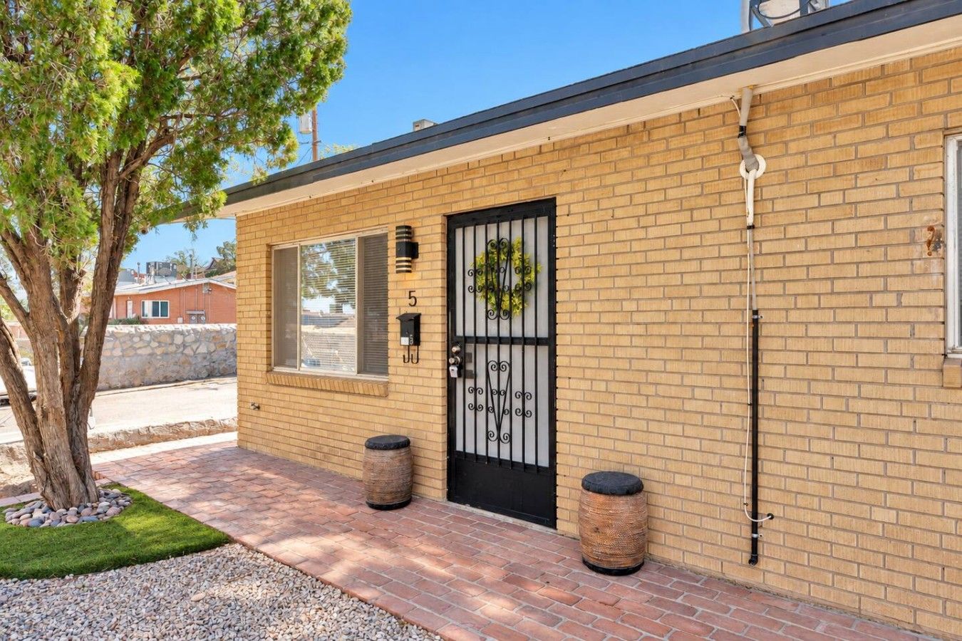 A brick building with a black metal gate, a small tree, and two cylindrical planters.
