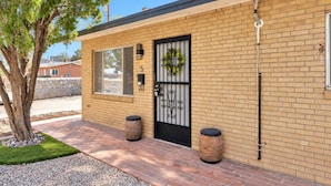 A brick building with a black metal gate, a small tree, and two cylindrical planters. - Central 2BR | Workspace, Laundry & Long Stays (El Paso)