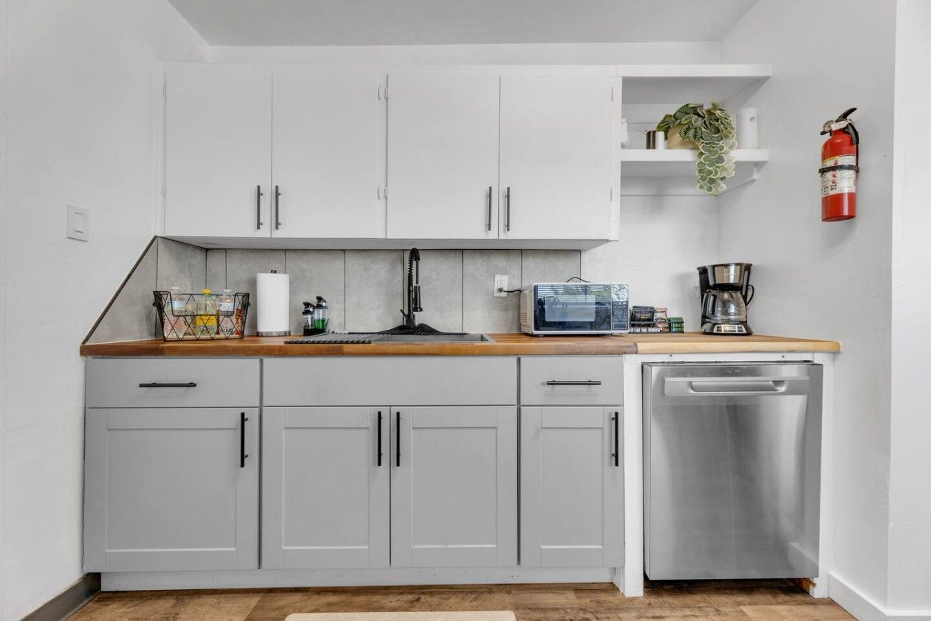 A modern kitchen with grey cabinets, a wooden countertop, a coffee maker, and a dishwasher.