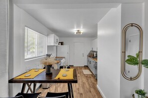 Une cuisine moderne avec des meubles blancs, un plan de travail en bois et un coin repas avec une table dressée pour deux personnes.