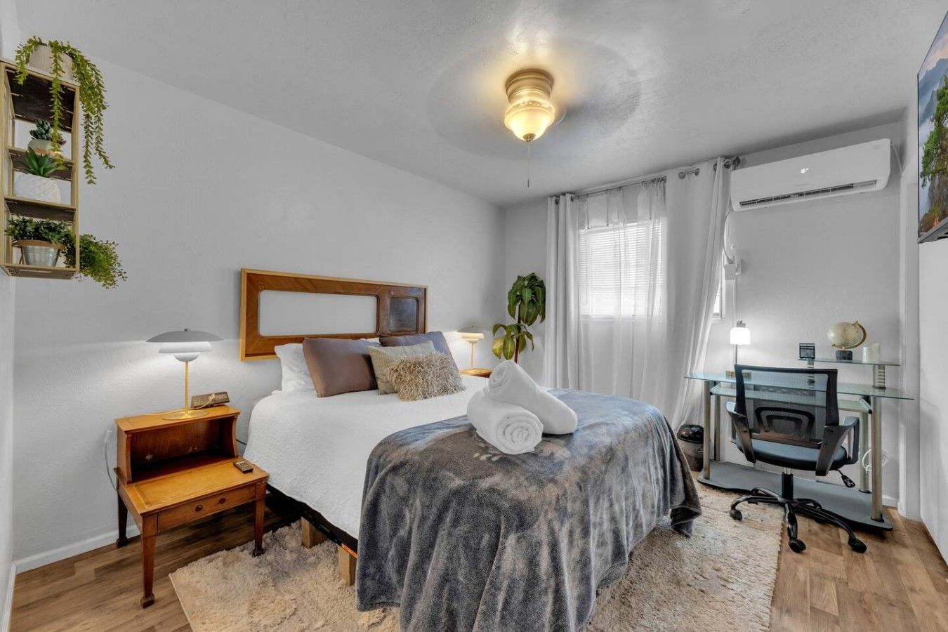 A bedroom with a bed, bedside table, lamp, and a desk with a chair.