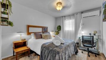 A bedroom with a bed, bedside table, lamp, and a desk with a chair.