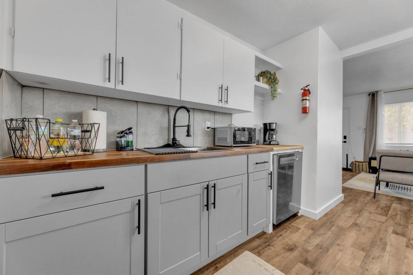 Una cucina moderna con mobili grigi, un piano di lavoro in legno, un lavello, un forno a microonde e una macchina per il caffè.